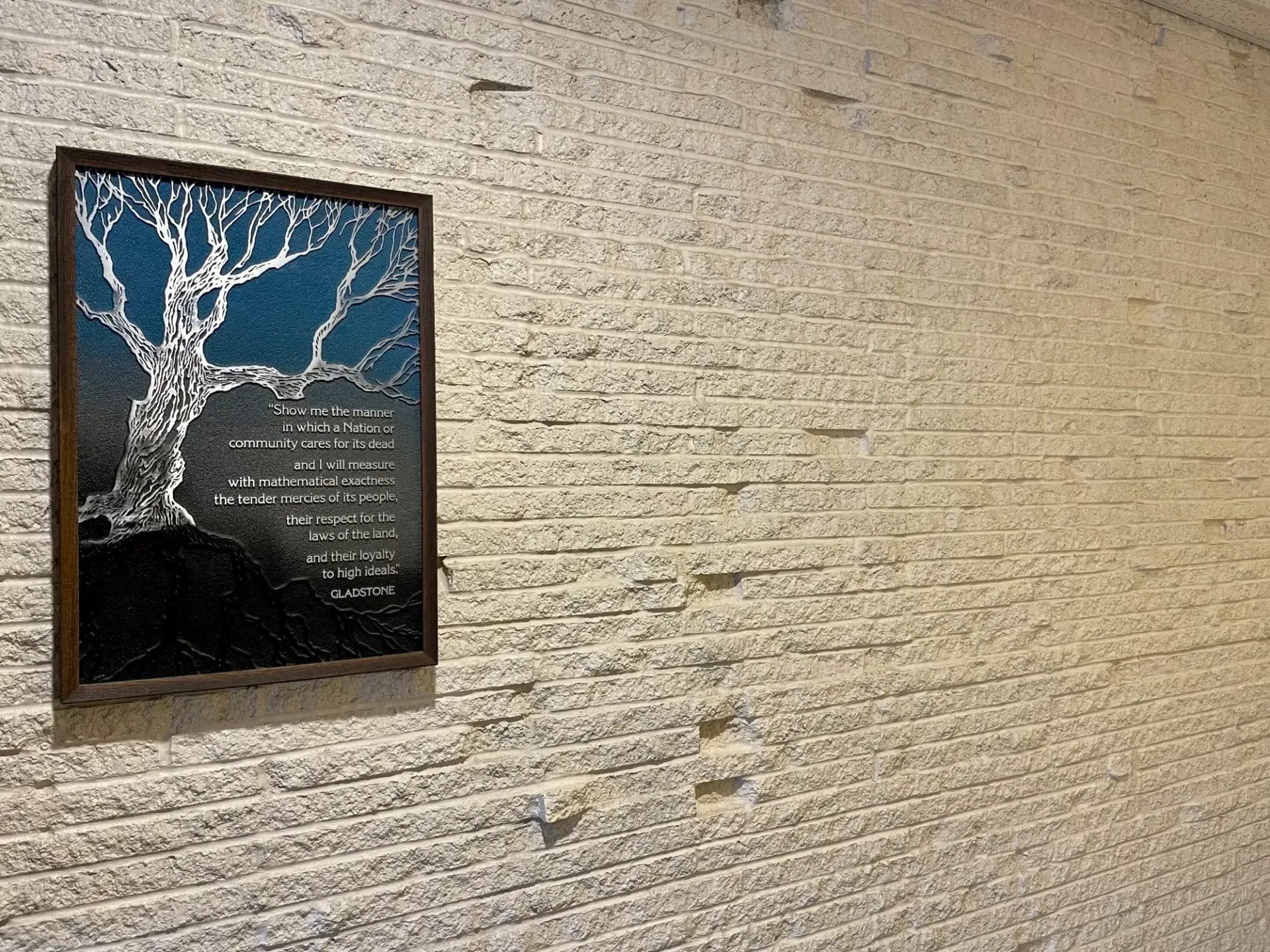 Framed plaque with a white tree on a beige brick wall in a dim hallway