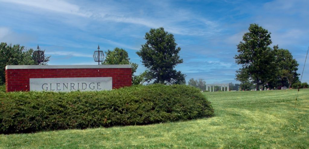Red Glenn entrance sign beside hedges and a green lawn under a blue sky