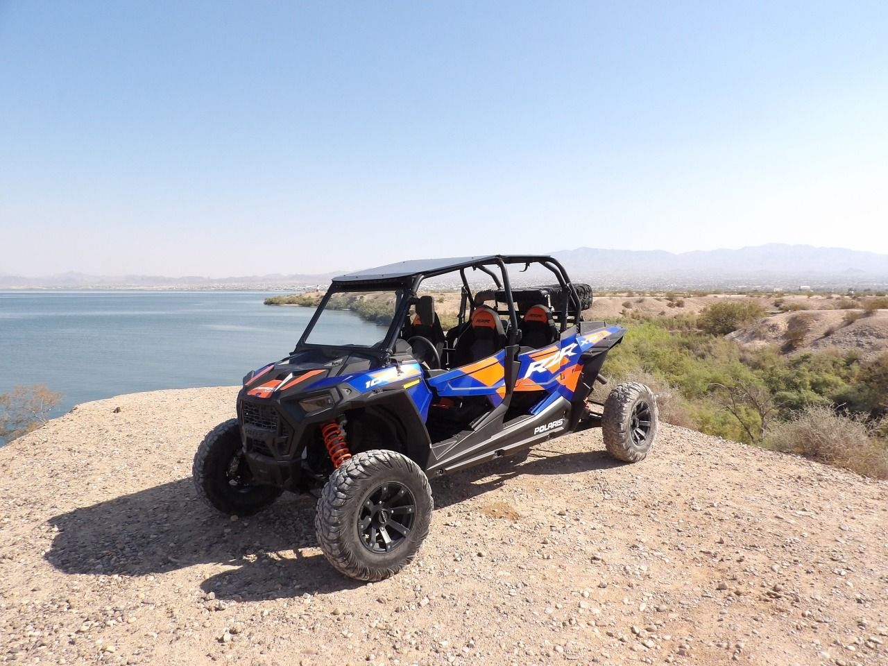 Blue and orange off-road buggy parked on a gravel overlook by a lake under a clear sky