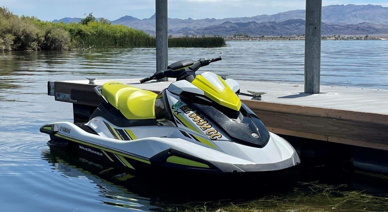Yellow and black jet ski docked beside a wooden pier on calm water with mountains in the distance