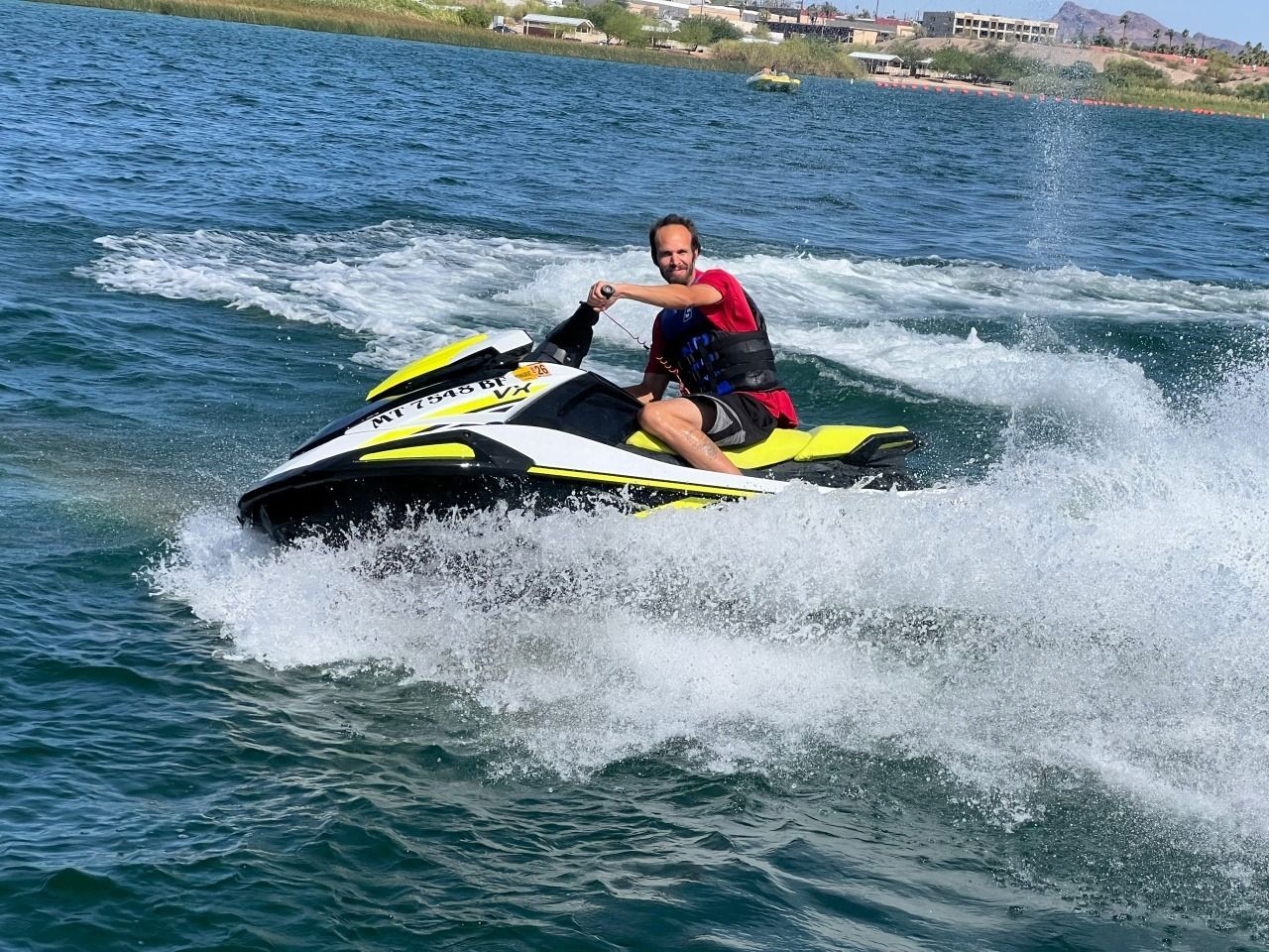 Person riding a black and yellow jet ski, splashing through blue water near the shore.
