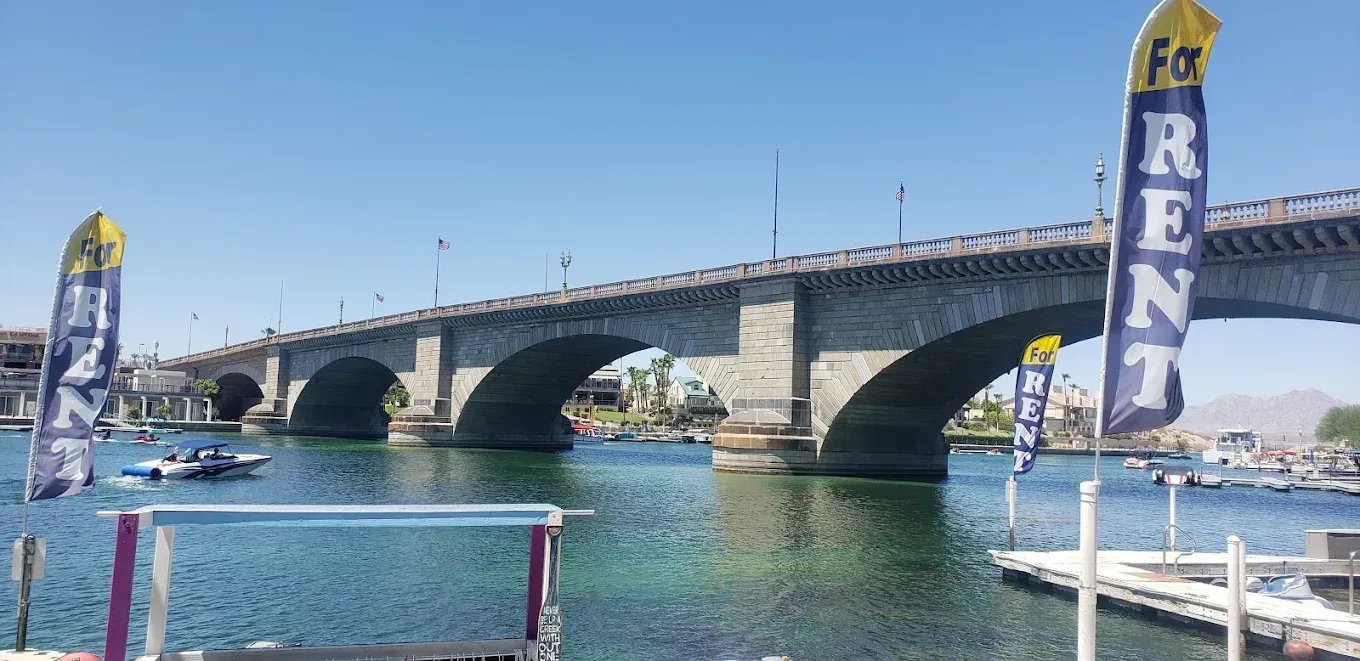 Stone bridge over turquoise water with sailboats and tall “REN” banner on the right