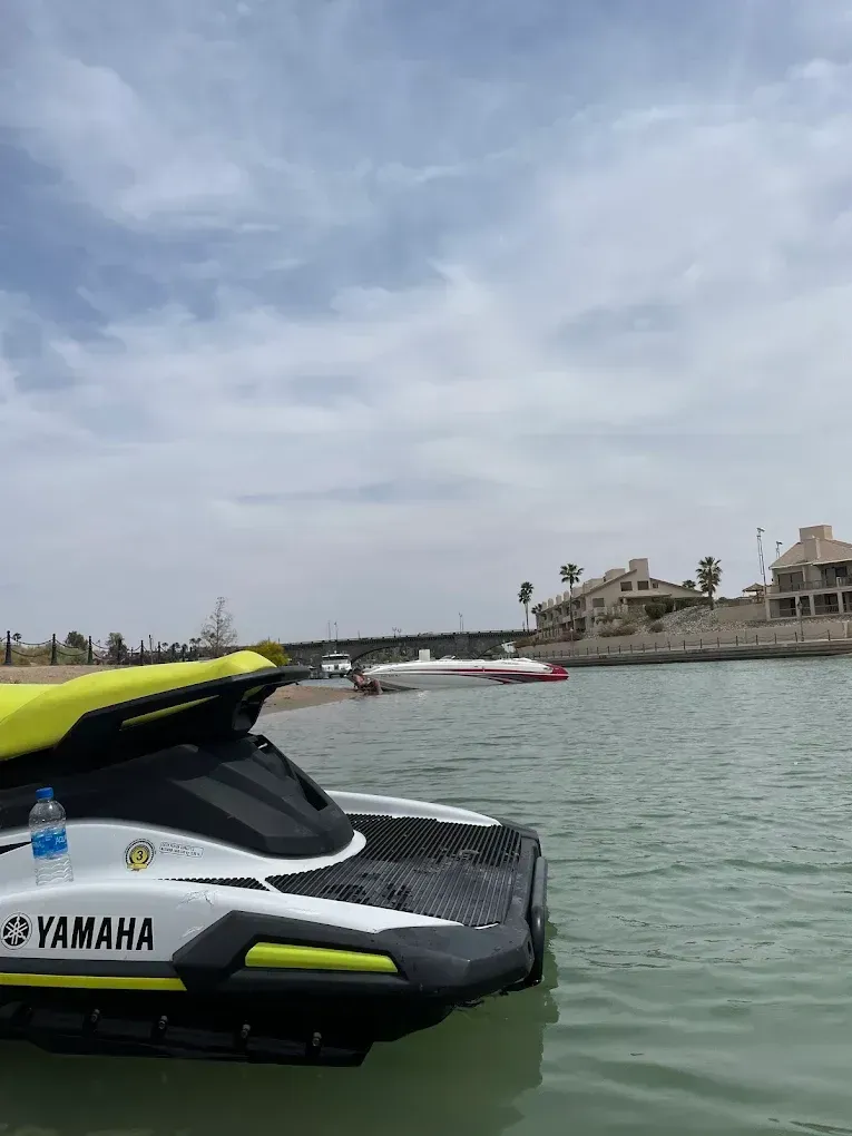 Yellow-and-black Yamaha jet ski on calm water near a waterfront with homes under a cloudy sky