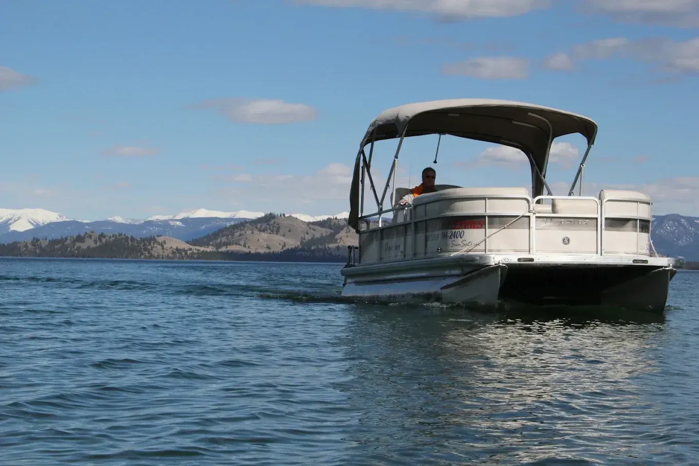 Pontoon boat cruising on a lake with snowy mountains in the background