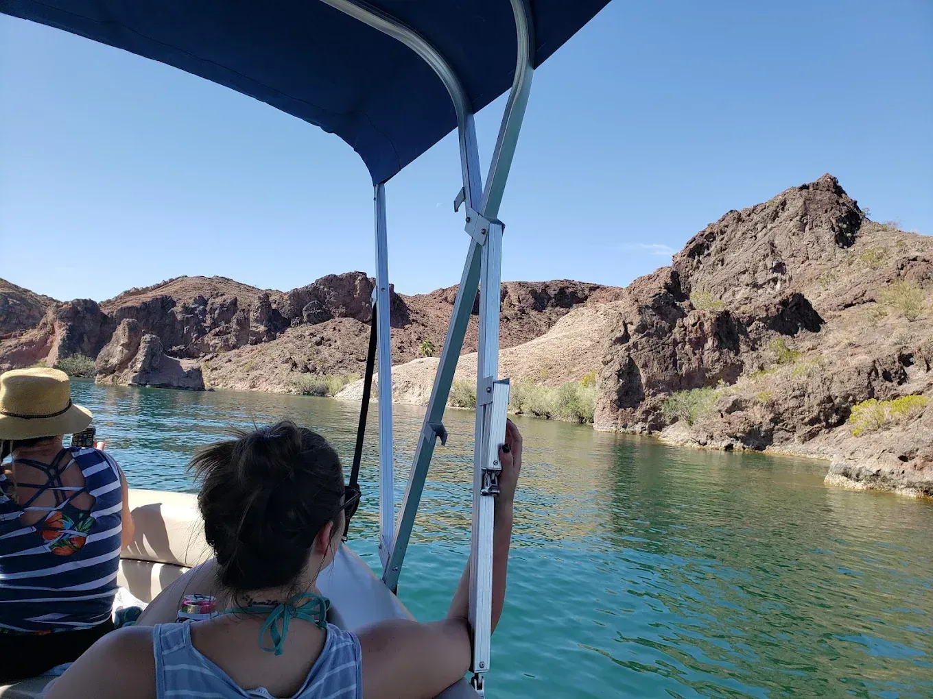 People on a boat looking at rocky desert cliffs and clear blue water under a sunny sky