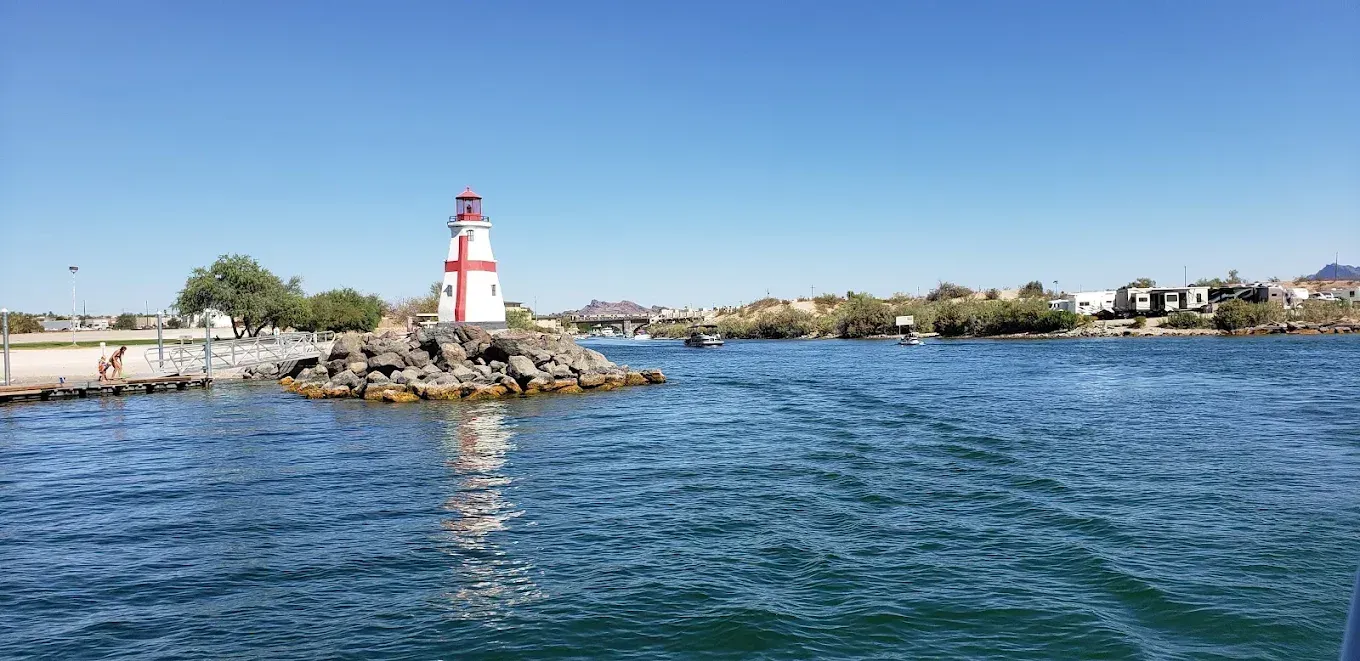 Red-and-white lighthouse on a rocky shore beside blue water under a clear sky
