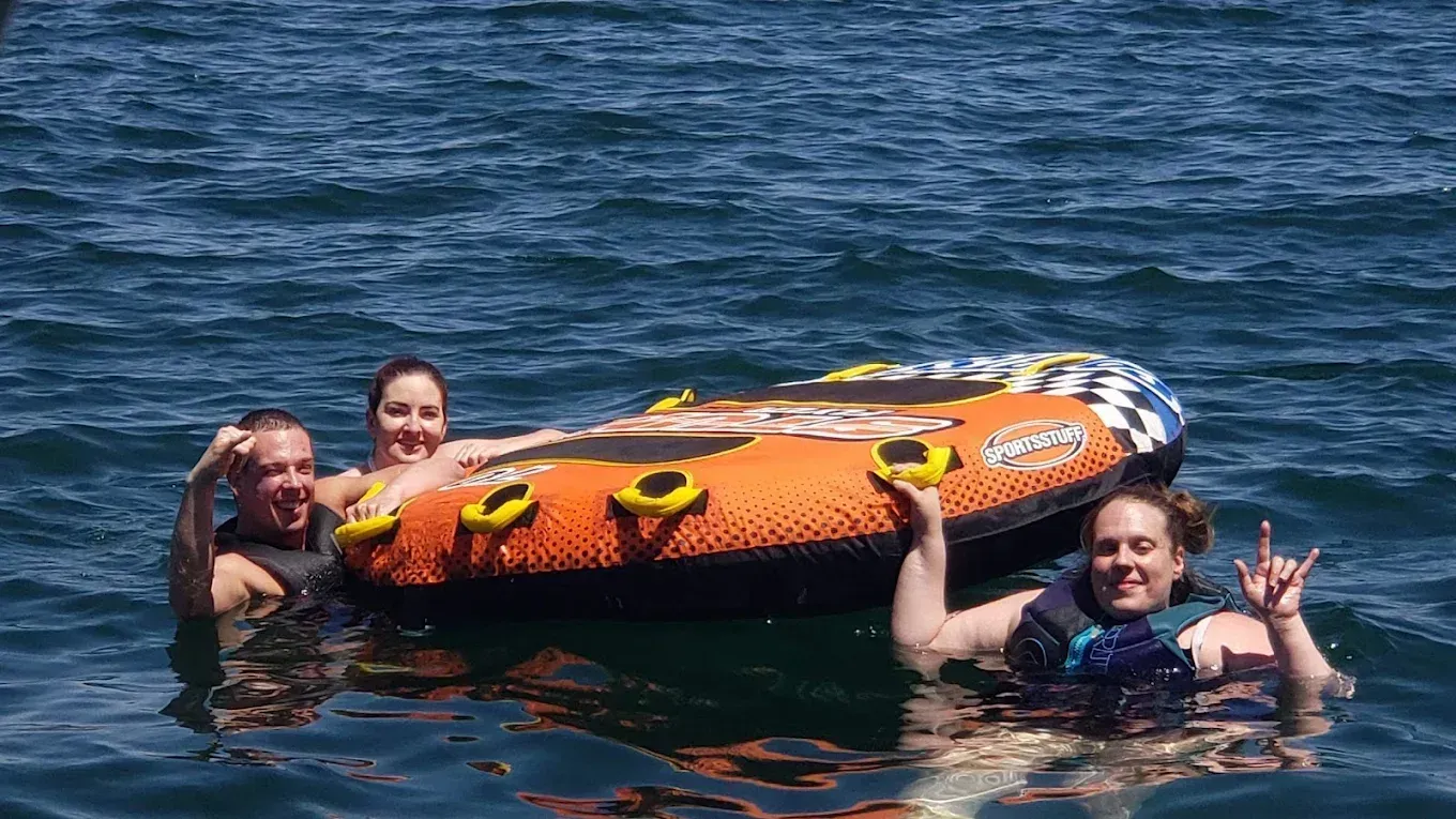 Three people in a lake holding an orange inflatable raft and smiling at the camera.