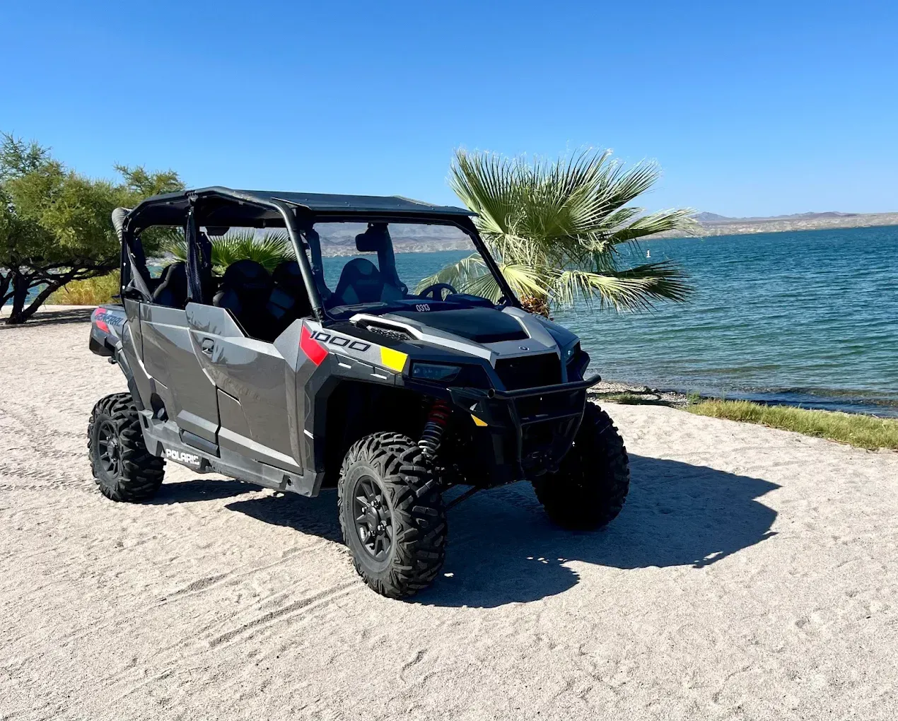Black off-road utility vehicle parked by a lakeshore with palm trees and blue water in the background