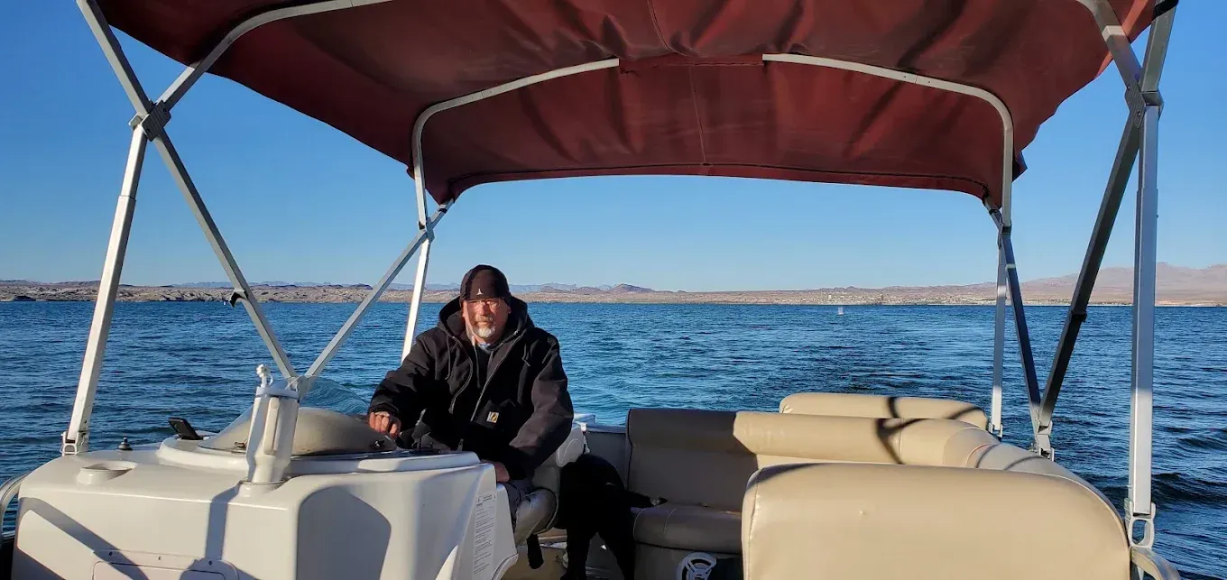 Person sitting on a boat under a red canopy on open water, with the blue sea and sky behind.