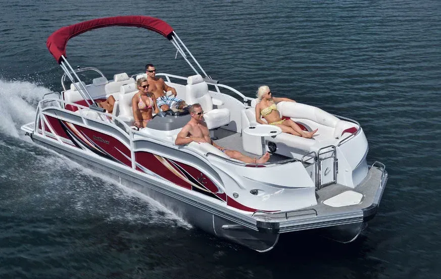 Five people lounging on a red-and-white pontoon boat speeding across calm water