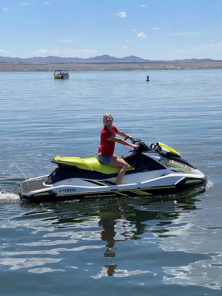 Person riding a yellow and black jet ski on calm water with mountains in the background
