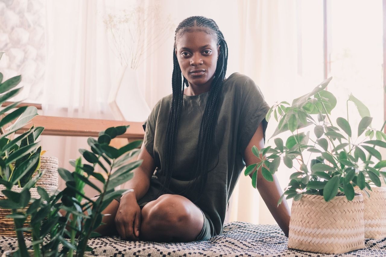 A Woman Is Sitting On A Bed Surrounded By Potted Plants