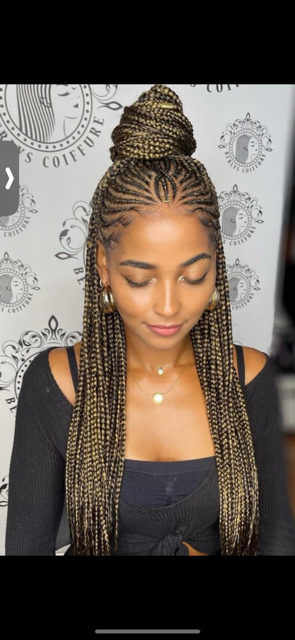 Woman with braided hair, a top bun, wearing a black top and gold jewelry.