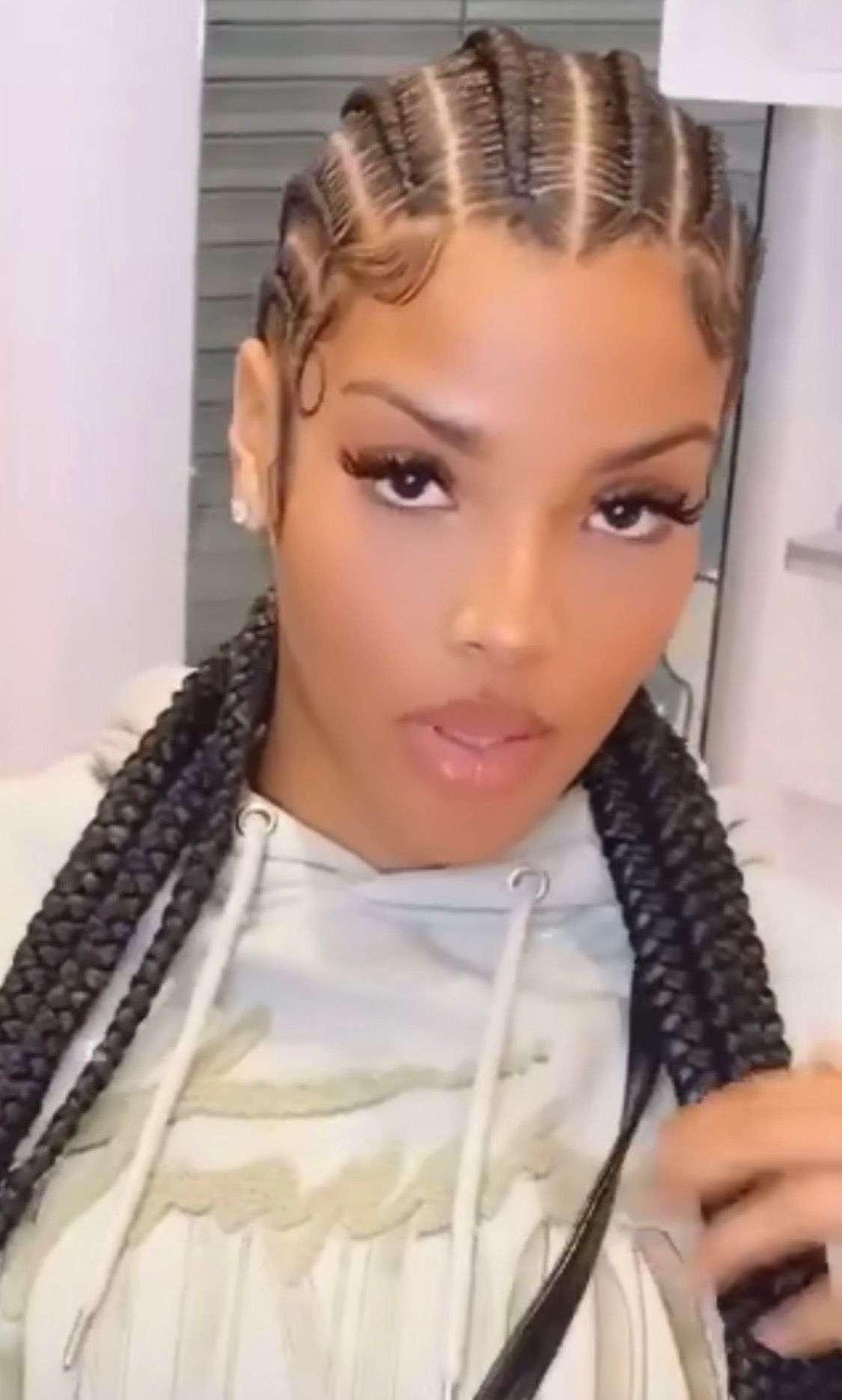 Woman with braided hairstyle, wearing a light-colored hoodie, looking at the camera.
