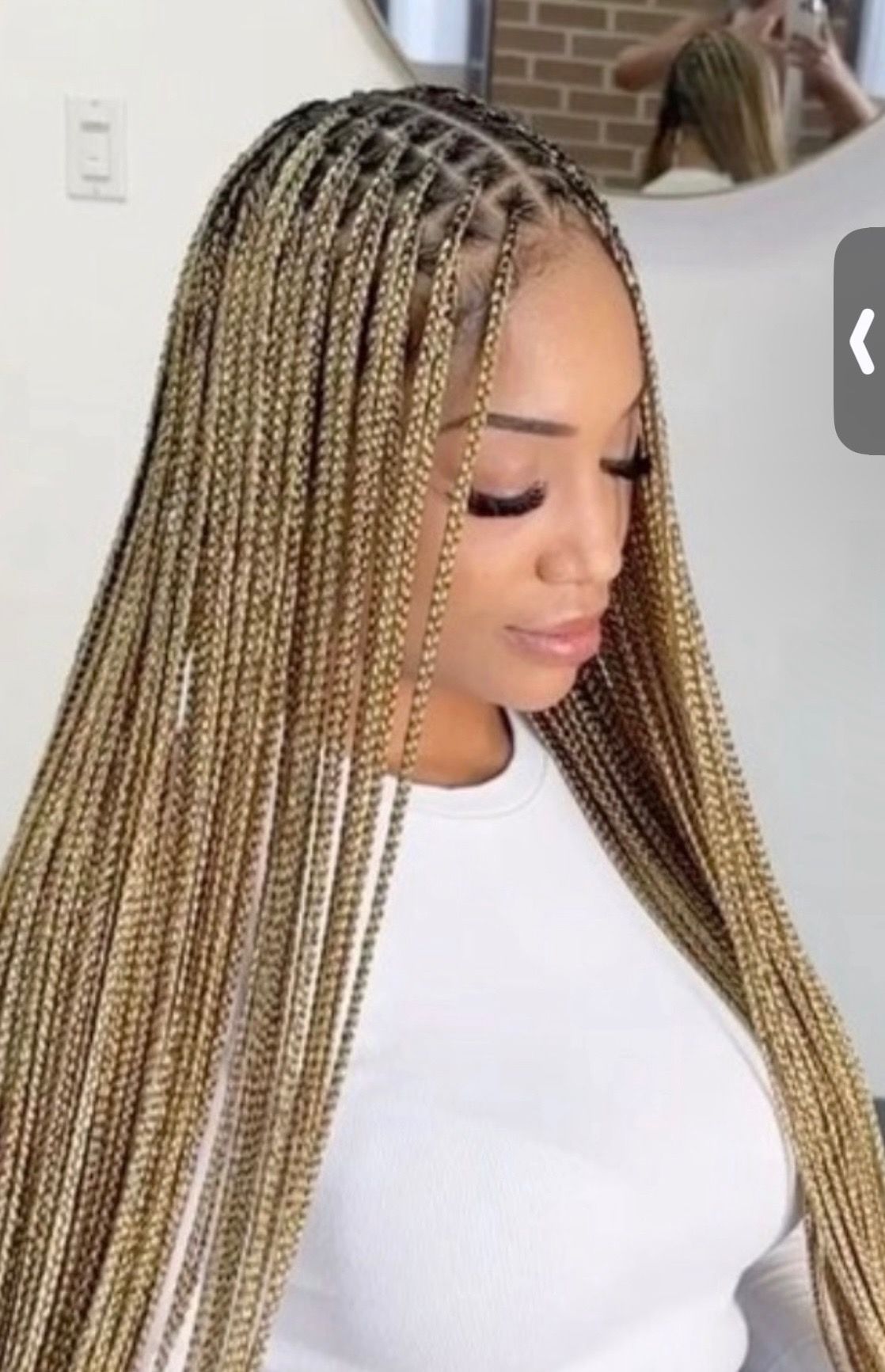 Woman with long, blonde and brown box braids, wearing a white shirt.