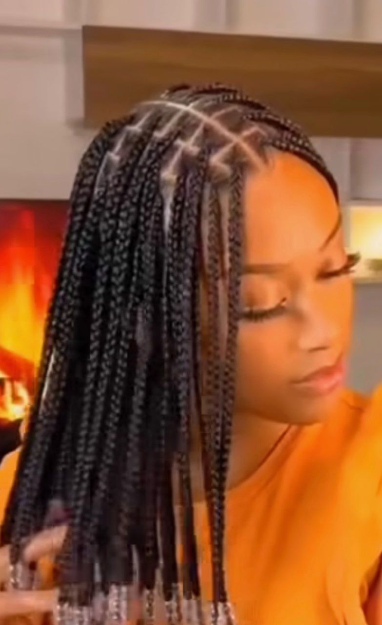 A woman with braids in her hair is wearing an orange shirt.