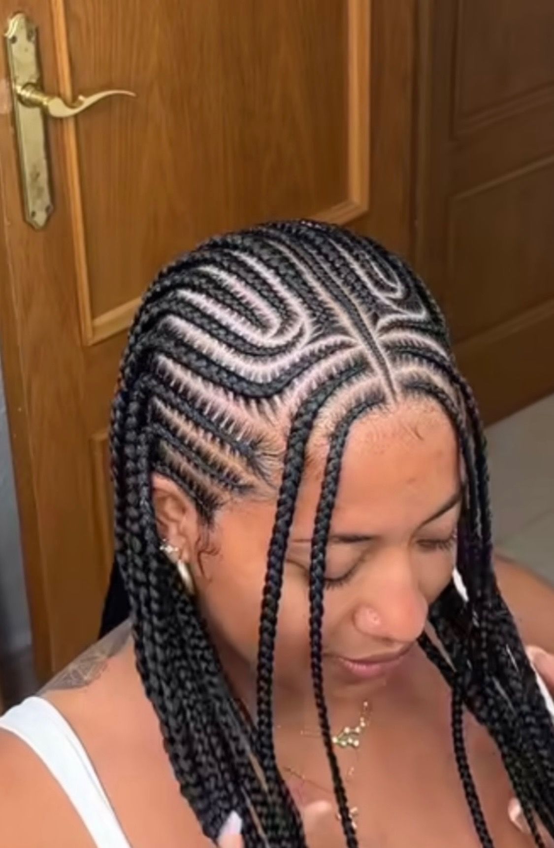 Woman with braided cornrows; curved design at the front; wearing a white top.