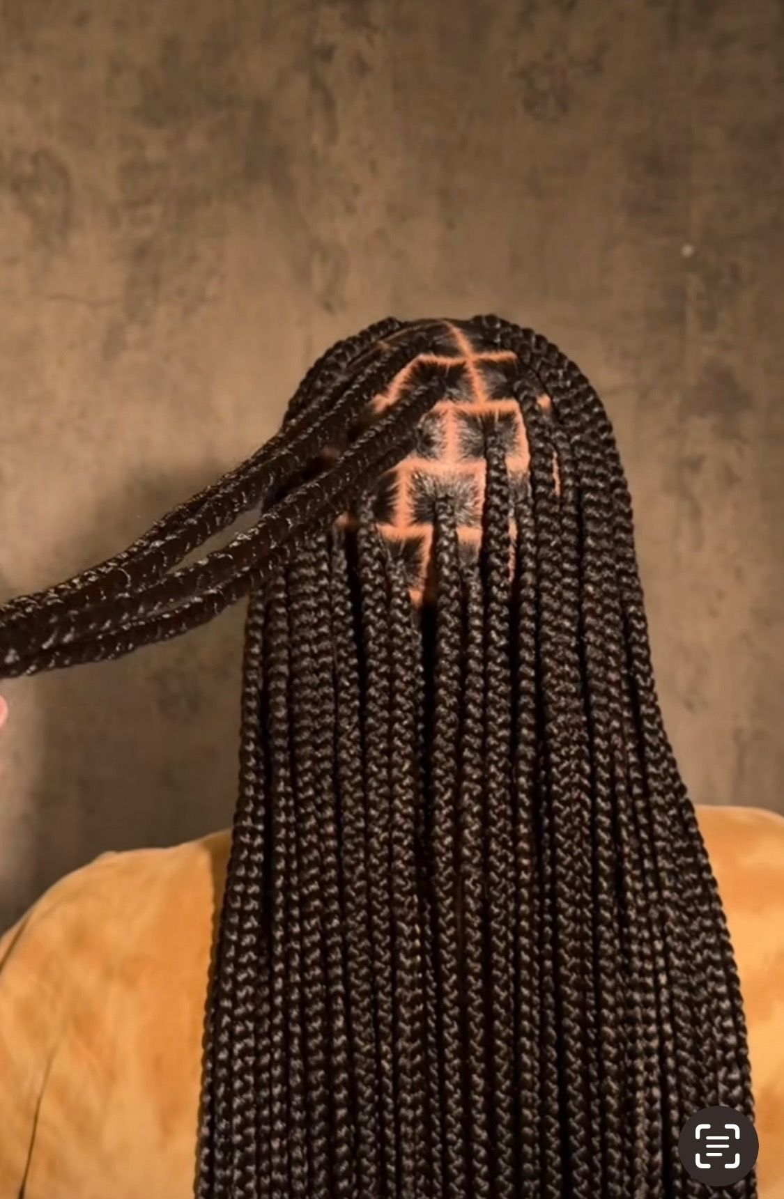Box braids hairstyle, dark hair, indoors. Hand holds a braid, showcasing the part and weave pattern.