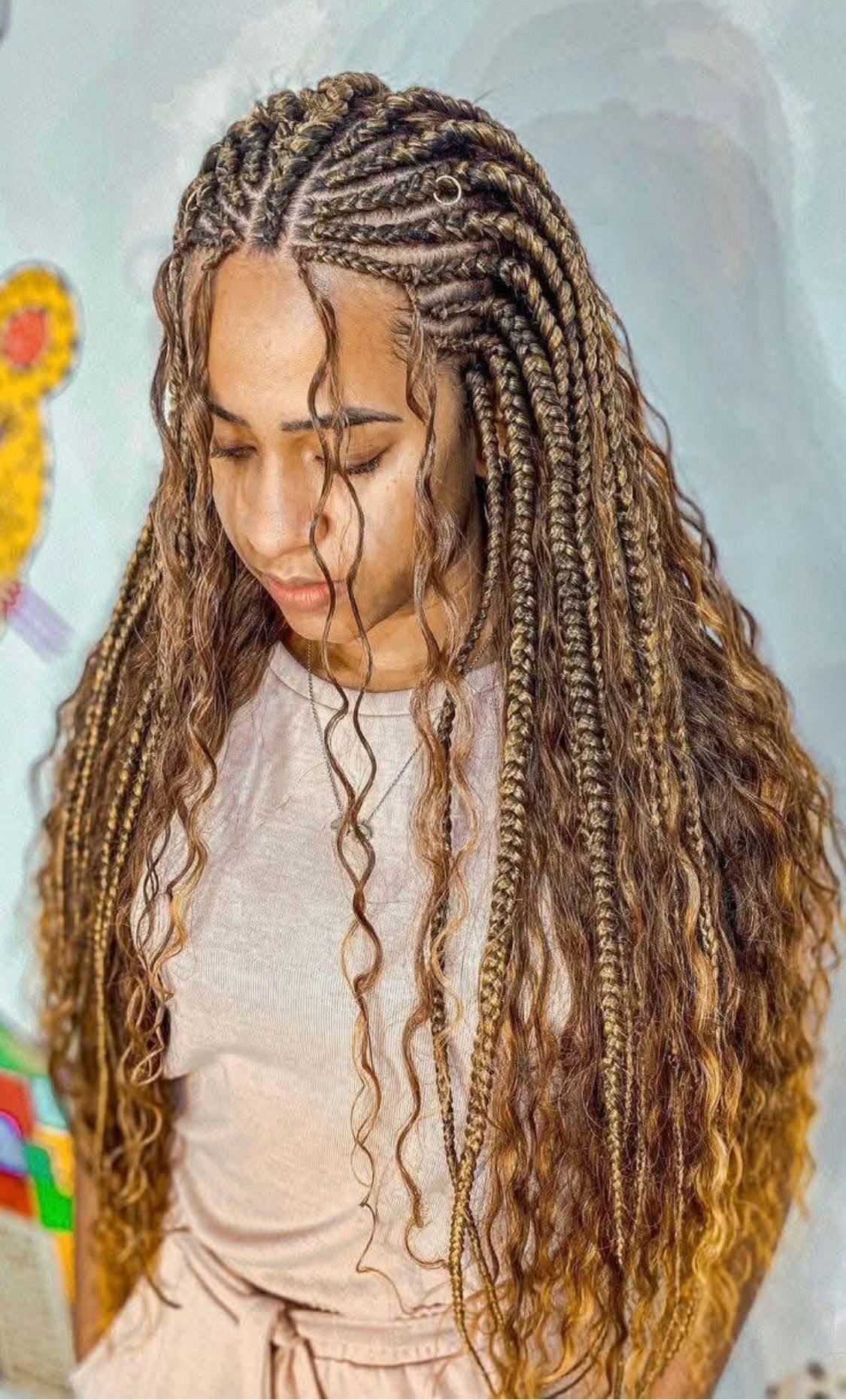 Woman with long, braided hair, some loose and wavy strands, in a room with a soft background.
