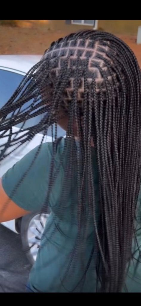 A woman with braids in her hair is standing in front of a car.