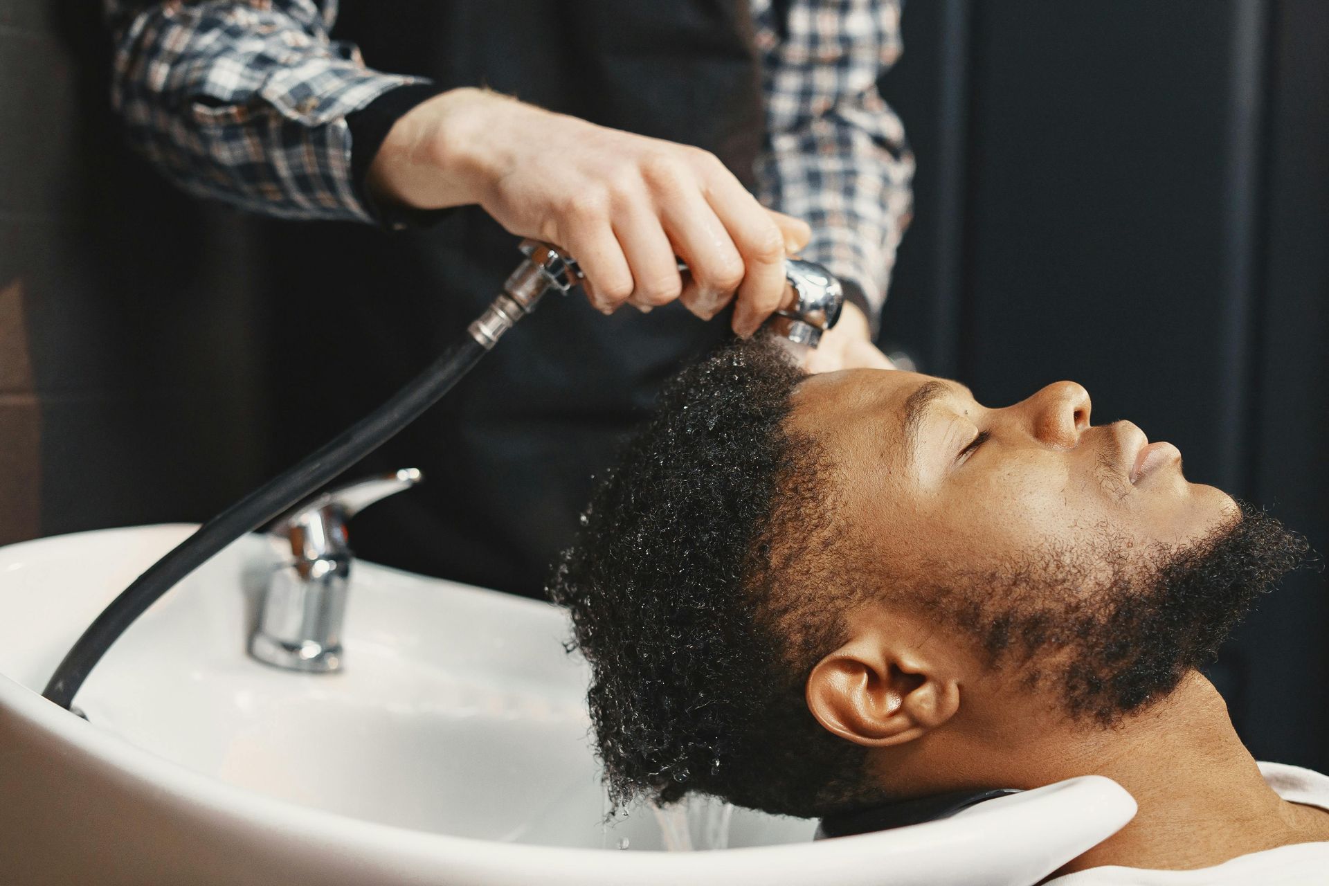 Man having hair washed at a salon, head tilted back in a sink, held by a person.