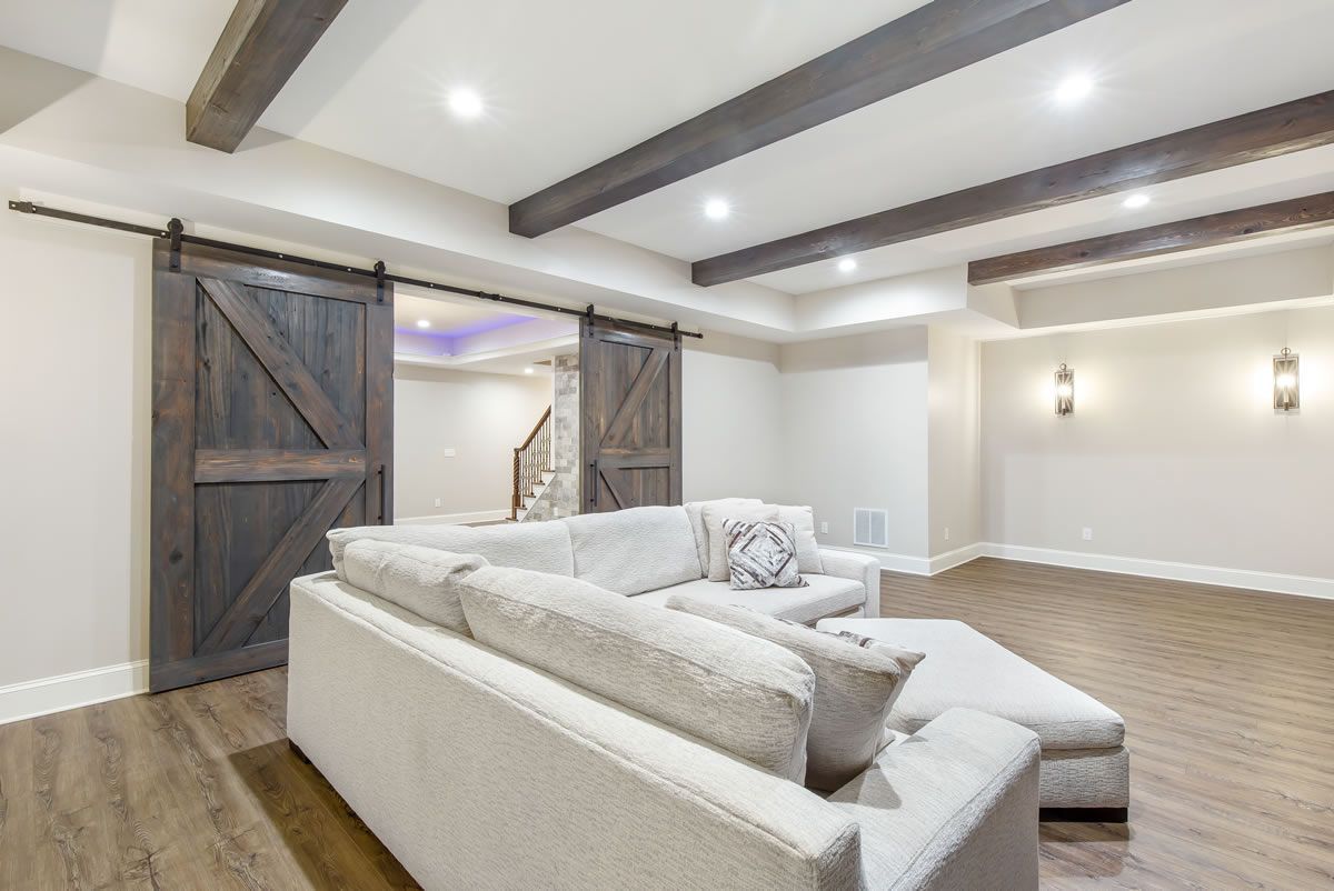 Living room with a large white sectional, wood barn doors, and dark wood beams.
