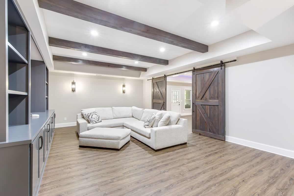 Modern living room with sectional sofa, built-in shelving, barn door, and wood beams.