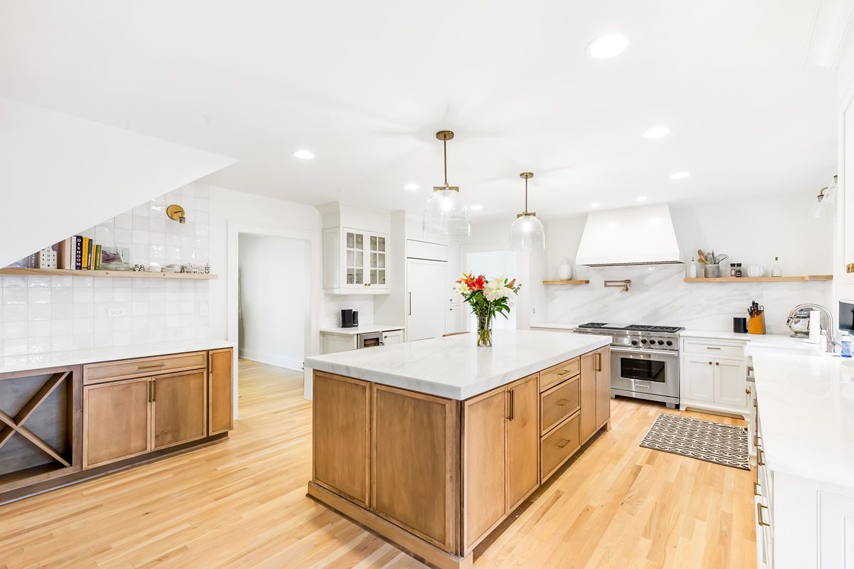 Modern kitchen with a large wooden island, white cabinets, white countertops, stainless steel stove, and hardwood floors.