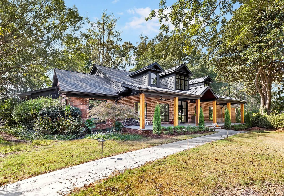 Brick house with black trim, wood columns, and porch under a shaded roof.