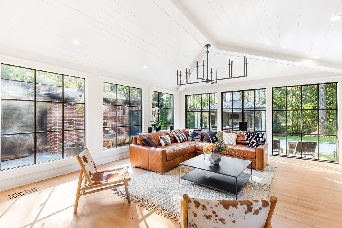 Living room with leather sectional, cowhide chairs, large windows, and a modern chandelier.