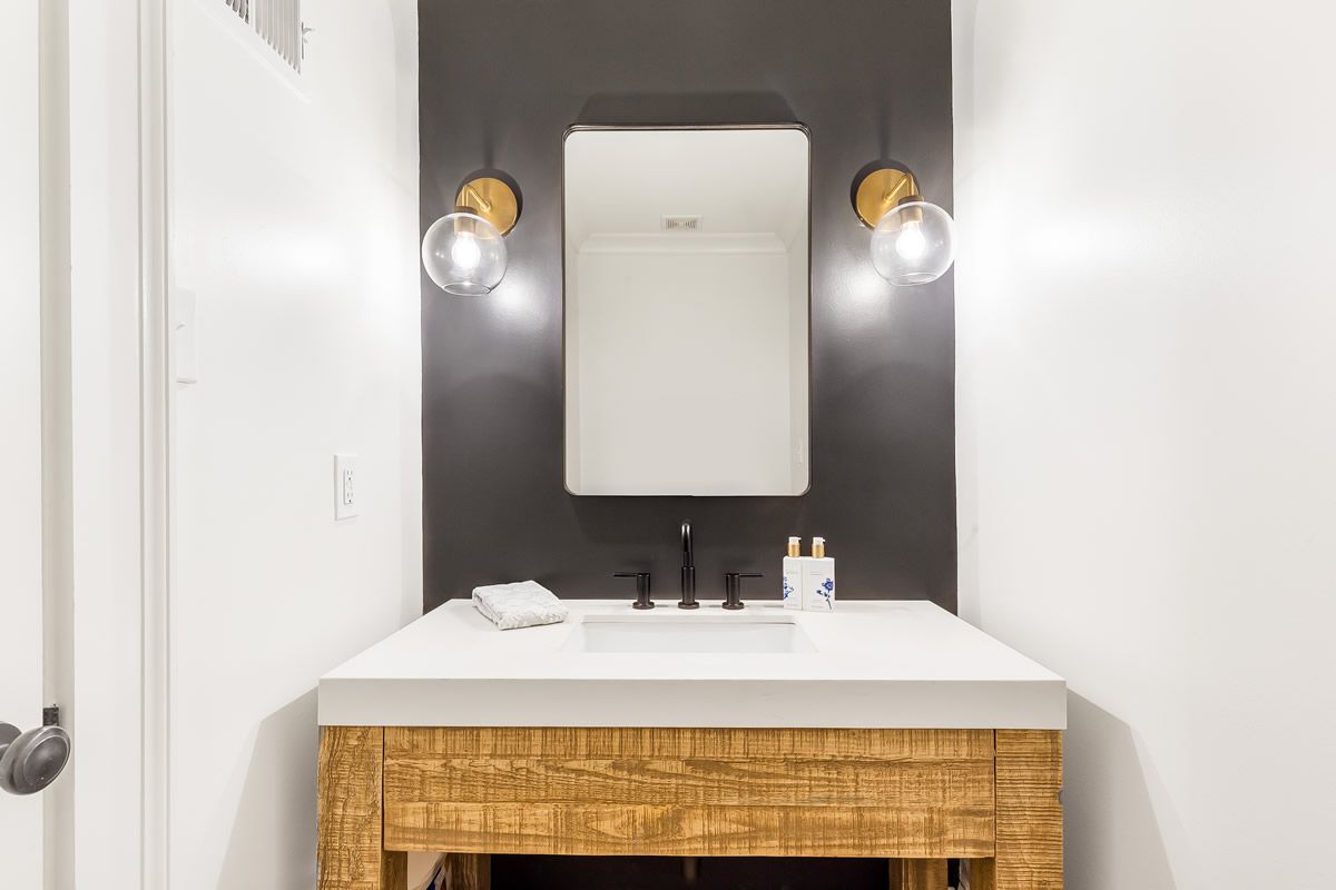 Bathroom with white countertop and sink, wooden cabinet, black faucet, mirror, and two globe sconces 