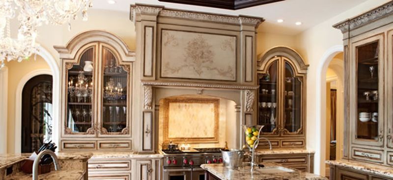 Kitchen with ornate cabinets, a range, and a decorative hood.  Neutral colors, elegant, and classic style.