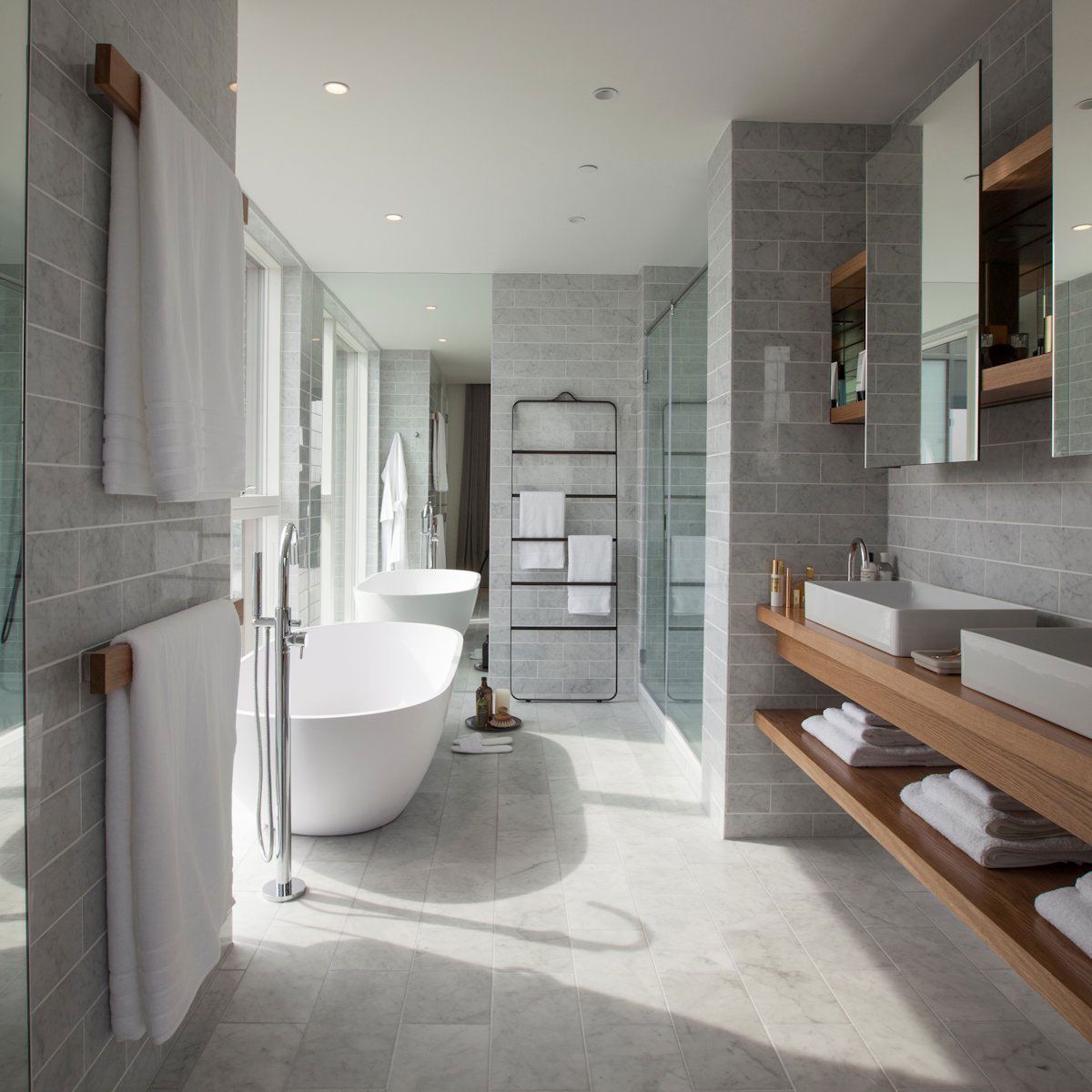 Modern bathroom with a white tub, grey tile walls, and wooden accents.