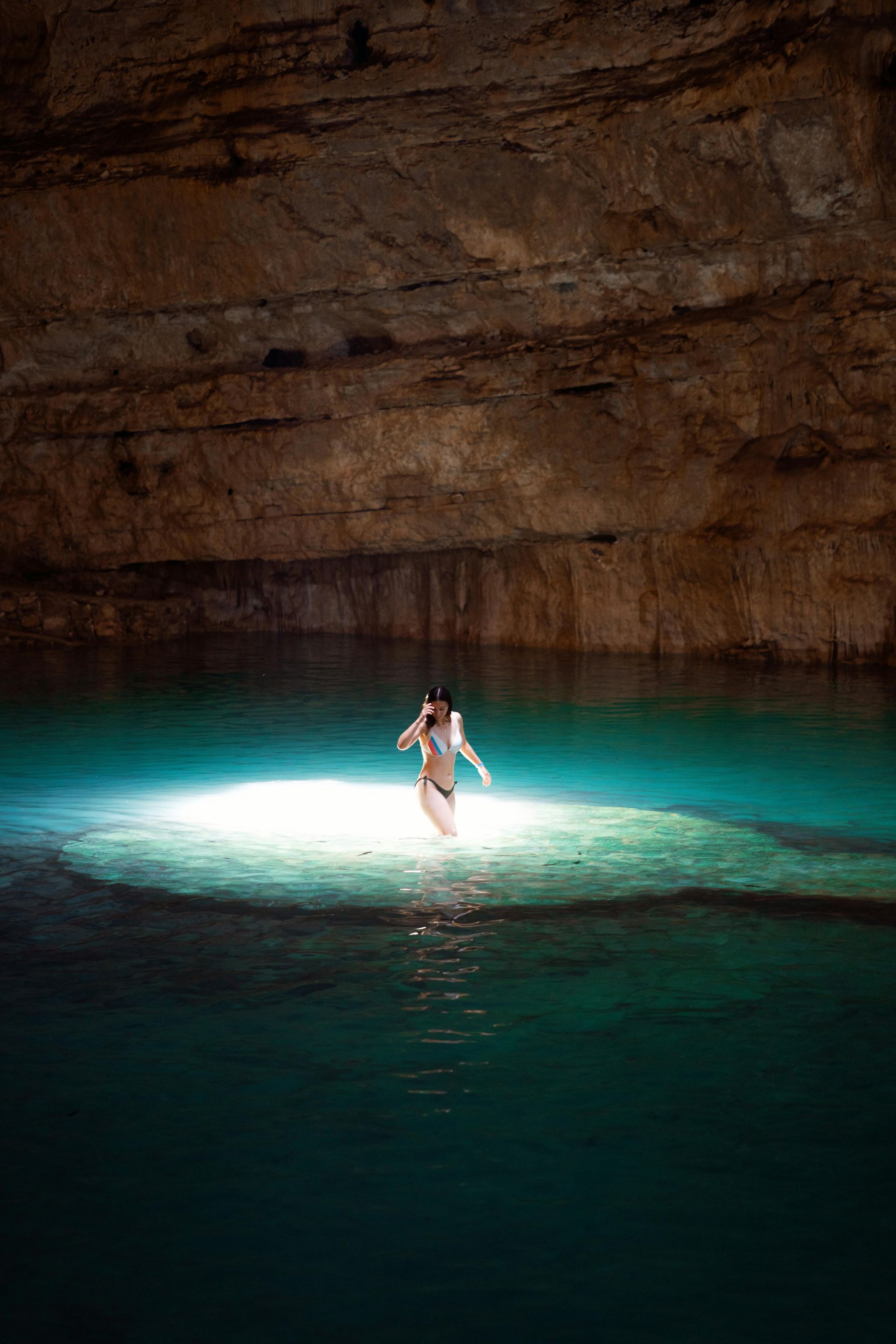 Persona de pie en una piscina turquesa brillante dentro de una cueva oscura.