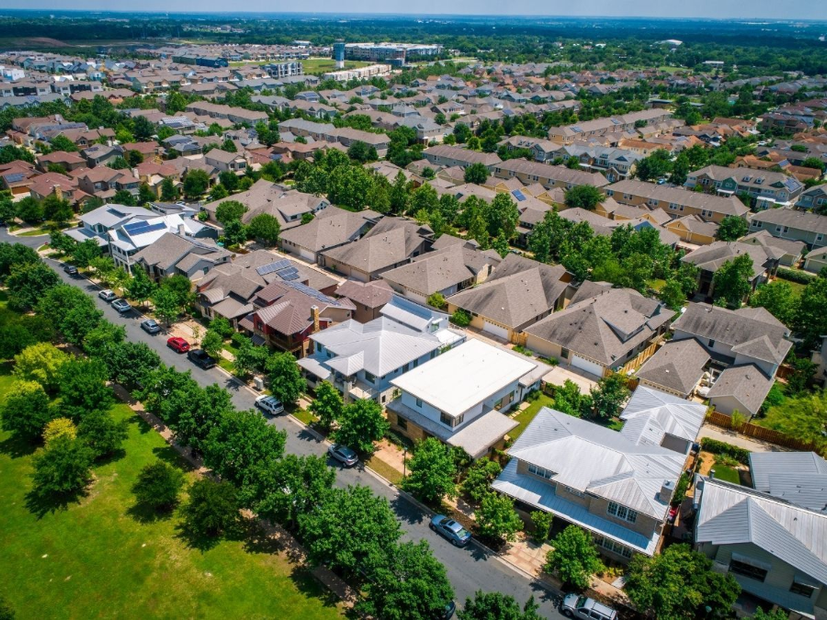 Aerial view of a suburban neighborhood with rows of houses, trees, and streets under a blue sky