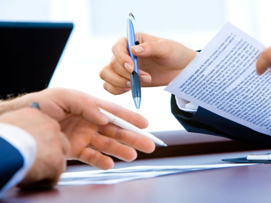 Hands exchanging a pen over paperwork at a desk during a business meeting