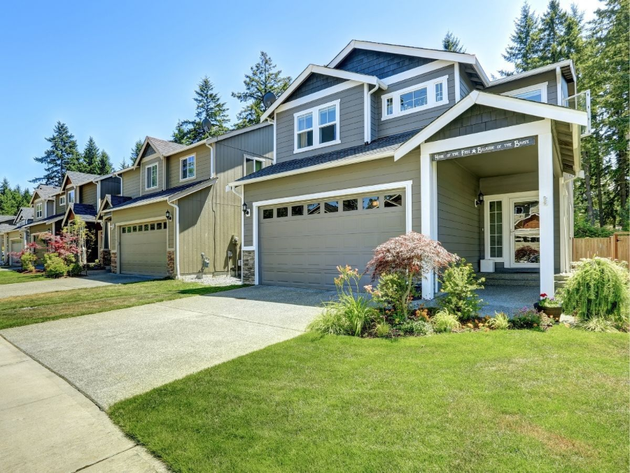 Suburban two-story house with gray siding, garage, and green lawn on a sunny day