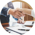 Two people shaking hands across a desk with a laptop and documents nearby