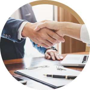 Two people shaking hands across a desk with a laptop and documents nearby