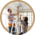 Two people on ladders installing a ceiling light in a bright room