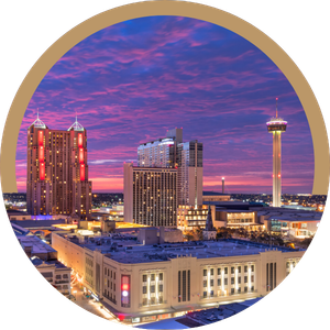 City skyline at sunset with colorful clouds, lit buildings, and a tall observation tower.