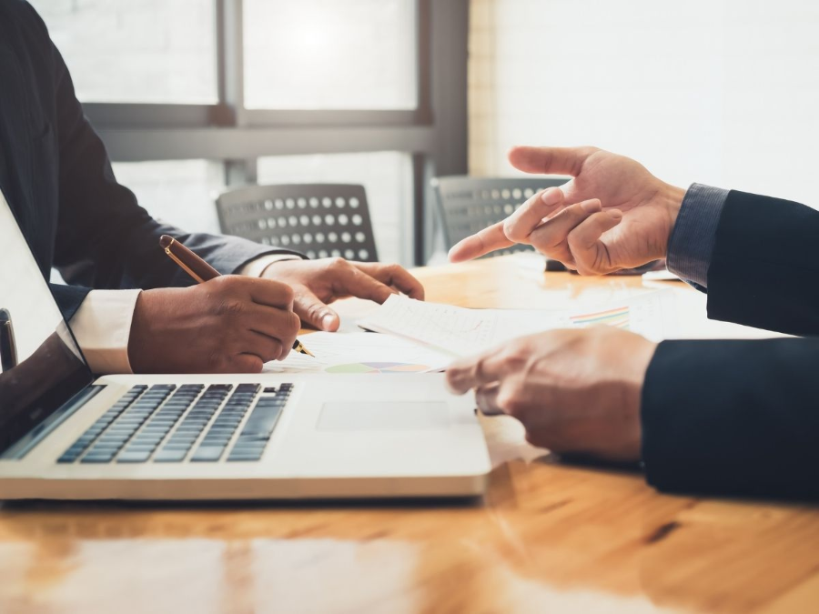People in a meeting discussing papers beside a laptop on a wooden table