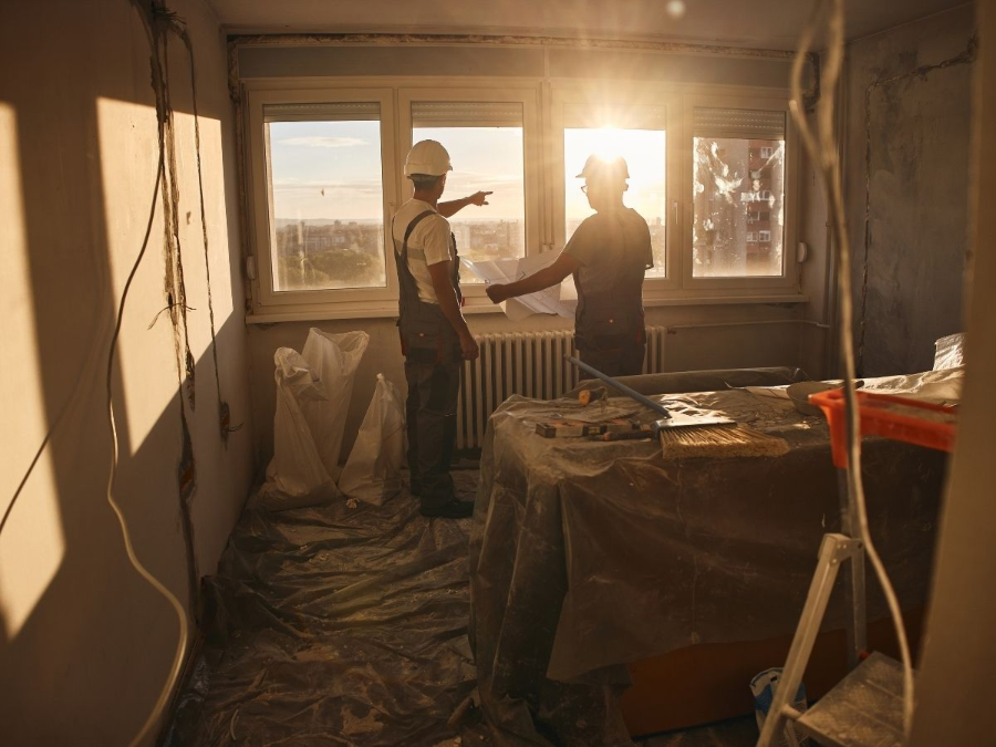 Two workers shaking hands in a sunlit room under renovation, with tools and covered furniture nearby