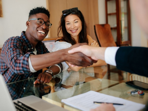 Two people shaking hands across a glass table during a meeting