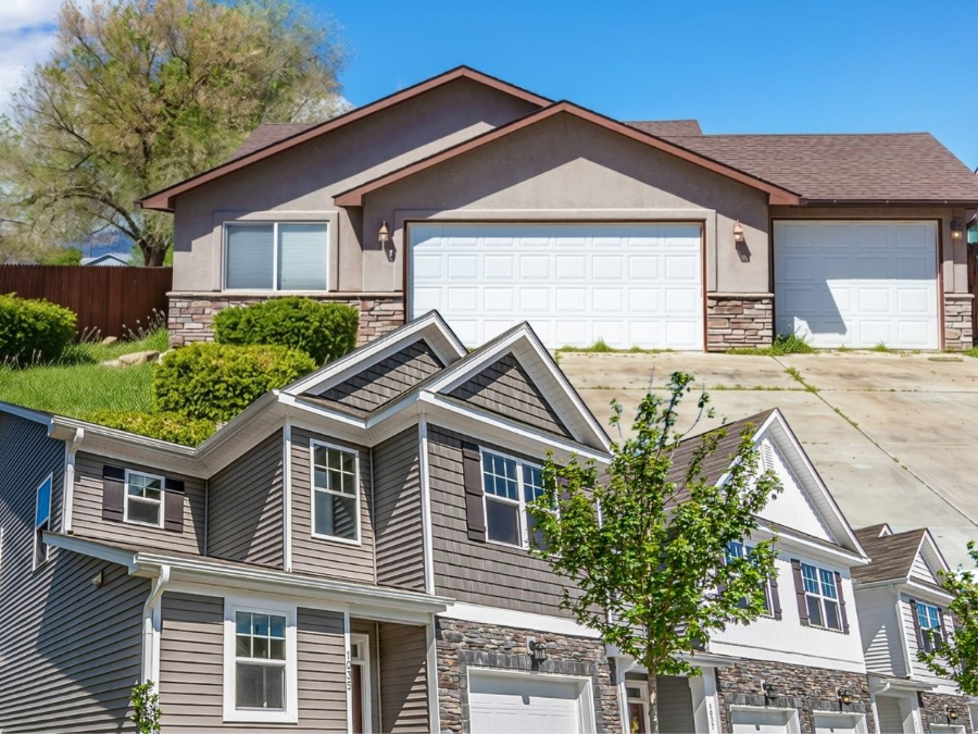 Two suburban houses, one beige and one gray, with garages and front lawns on a sunny day