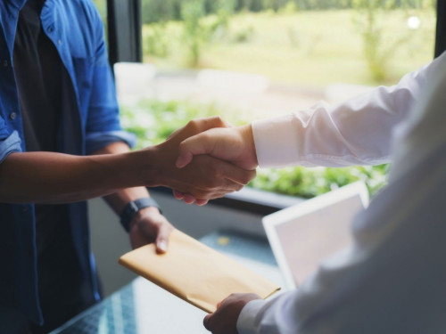 Two people shaking hands near a window, with a folder in hand