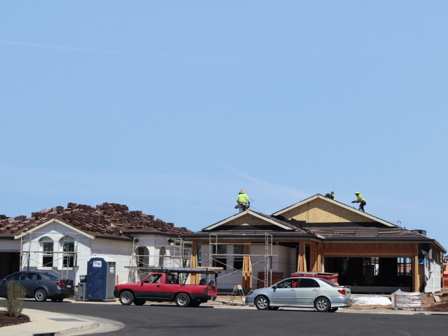 Residential street with two houses, parked cars, and workers on the roof under a clear blue sky
