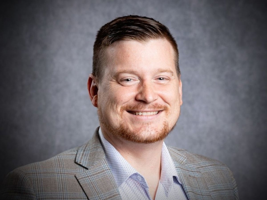 Smiling man in a light gray blazer against a gray studio backdrop