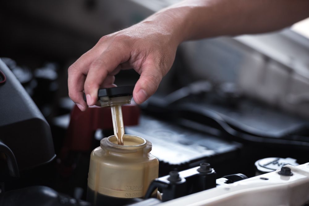 A Person is Pouring Oil Into a Bottle Under the Hood of a Car — Brittle's Family Auto Centre in Moffat Beach, QLD