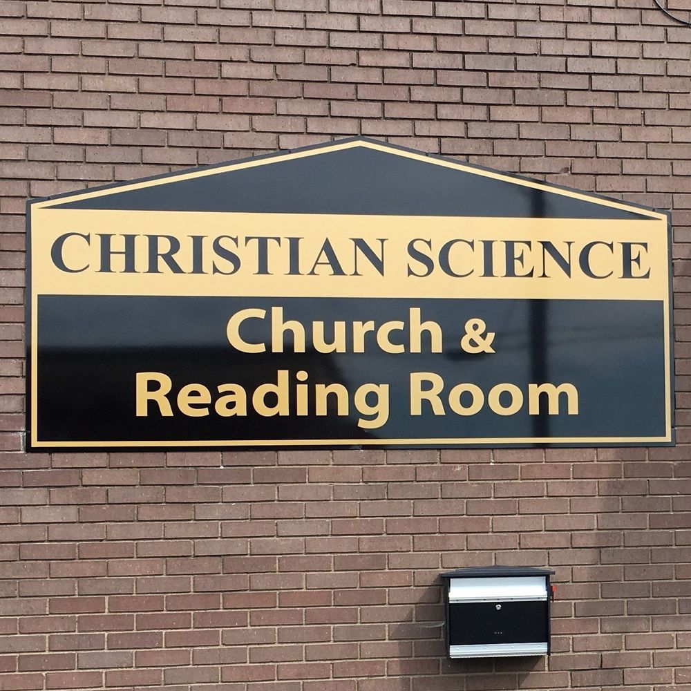A sign on a brick wall says christian science church & reading room